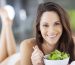 happy young woman eating salad on bed